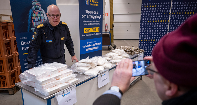 Han står vid ett bord. På bordet ligger många påsar med droger.