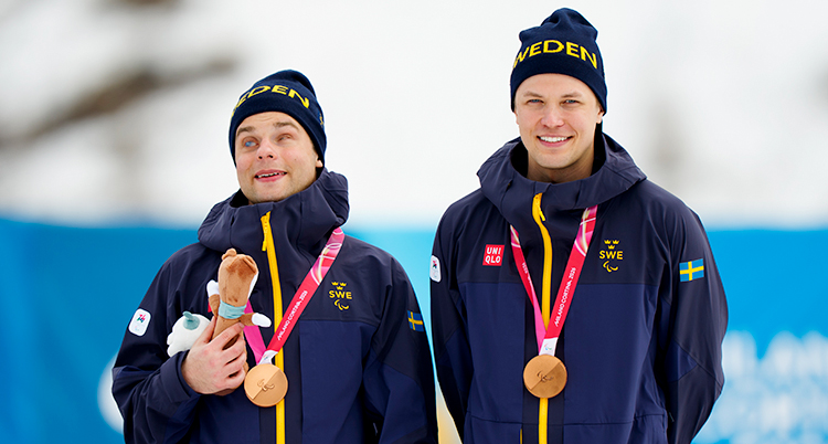 De är glada. De står bredvid varandra. De har fått varsin medalj.