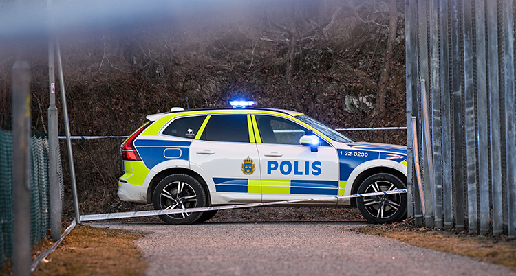 En polisbil med blåljus står bakom polisernas band.