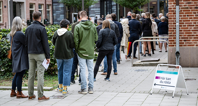 Människor står i kö utanför en skola. Inne i skolan kan man rösta.