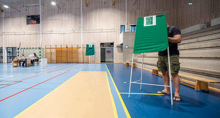En gymnastiksal. Där finns gröna bås där folk kan rösta.