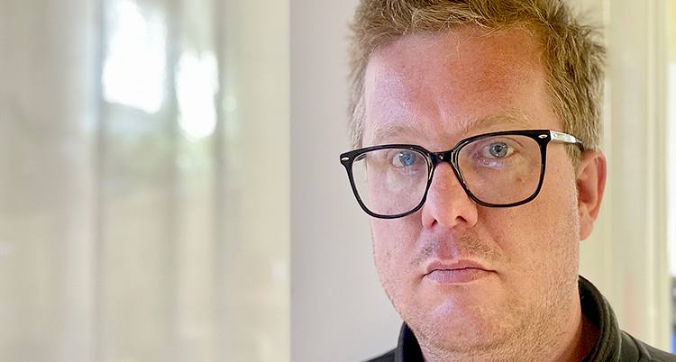 Han har glasögon med svarta bågar och ljust hår som står upp.