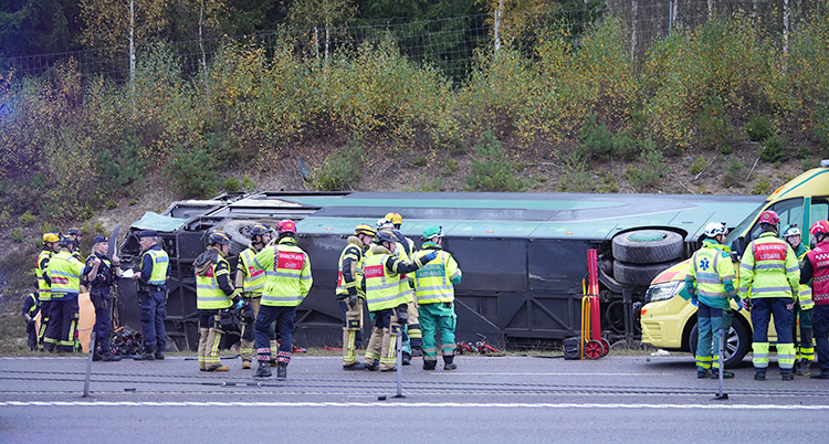 En buss ligger bredvid en väg. Runt den står poliser och personer från räddningstjänst och ambulans.