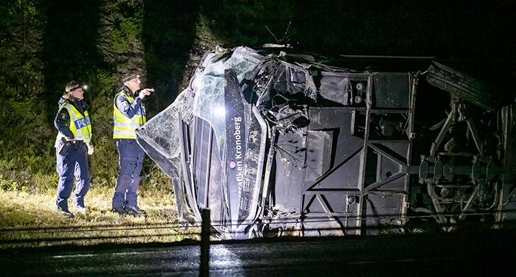 Det är mörkt ute. Två poliser lyser med ficklampa på bussen som har vält.