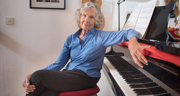 Hon sitter vid ett piano.