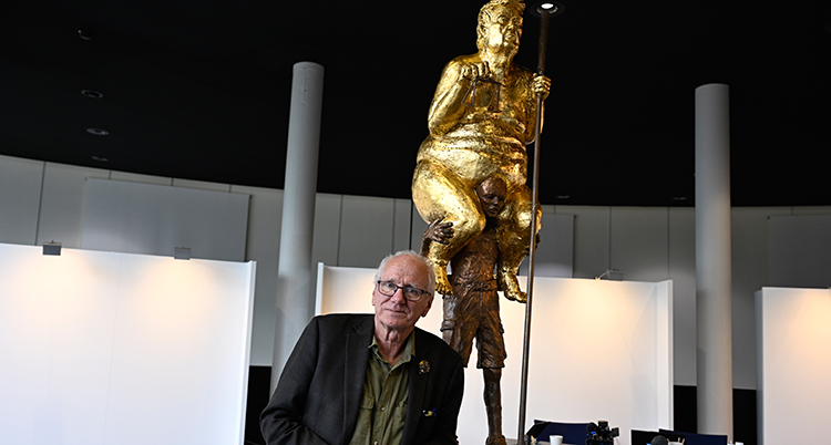 En staty i guld där en stor naken kropp sitt på en pojkes axlar.