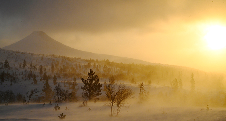 En fjälltopp och en sol på en molnig himmel.
