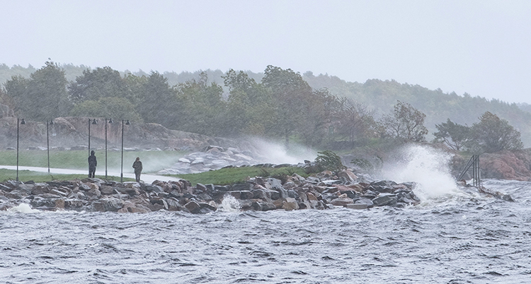 Det blåser vid havet. Två personer går vid stranden.