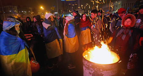 Demonstranter i Kiev värmer sig vid en eld. Foto: Sergej Grits/TT.