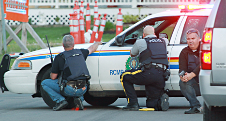 Poliser gömmer sig bakom en bil när de försöker fånga mördaren. Foto: Moncton Times /Ron Ward /TT