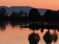 En rosa himmel syns bakom fjället och speglar sig i en blank sjö