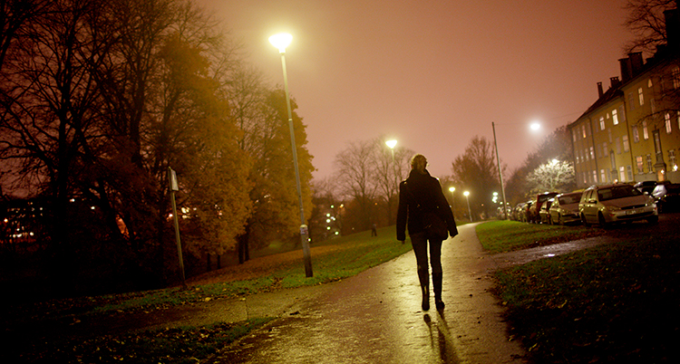 Det är mörkt ute. En kvinna går på en gångväg.