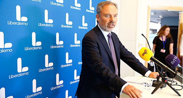 Jan Björklund står framför en vägg täckt av bokstaven L som är partiets nya symbol. Bokstaven är vit på blå botten och har rundade kanter.