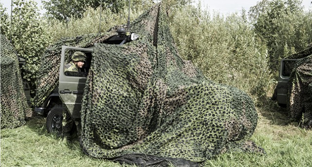 Militärer gömmer sig bakom ett grönt skydd ute i naturen.