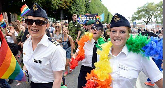 Kvinnor från försvarsmakten har på sig uniformer och runt halsarna har de varsin färgglad fjäderboa i regnbågens färger.