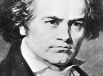 En svartvit bild på Ludwig van Beethoven. Han ser sträng ut. med lätt rynkade ögonbryn och ganska rufsigt hår som hänger ner över öronen. Han har en vit skjorta med krås och en svart kavaj.