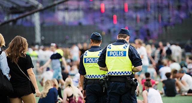 Poliser går runt på ett område för en musikfestival. På gräset sitter många människor.