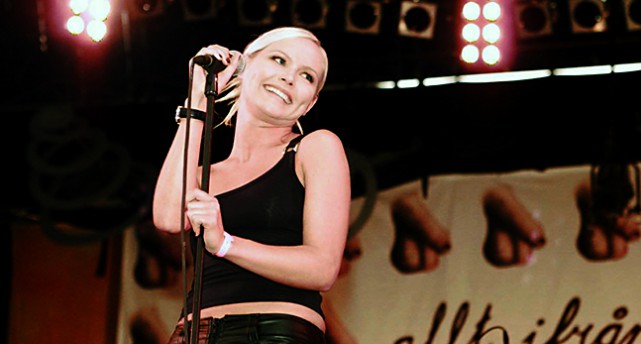 Nina Persson håller i en mikrofon och ler.