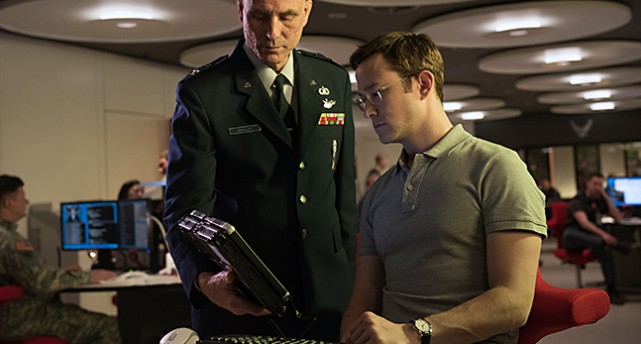 Bild från filmen. En man med militära kläder står visar något på en dator för Edward Snowden.