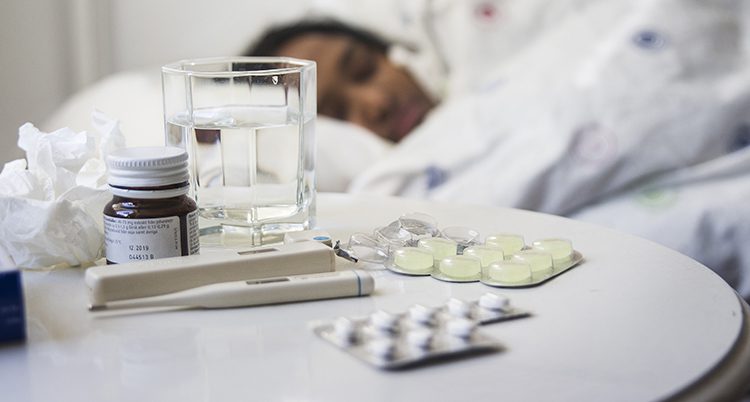 En kvinna i en säng med mediciner på ett bord bredvid sig.
