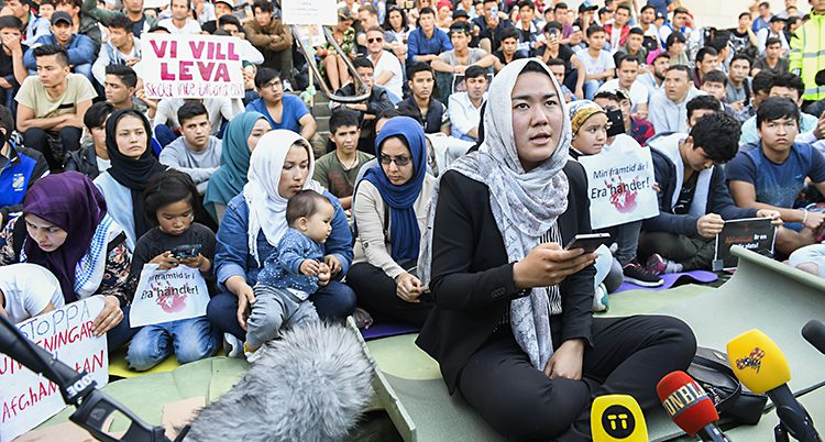 Unga flyktingar sitter på en trappa med plakat