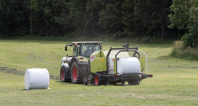 En traktor med bakar abv av hö på en åker