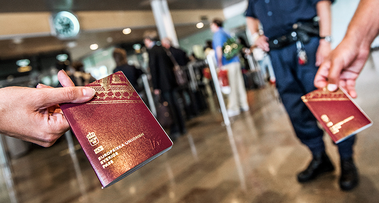 Två händer håller fram varsitt pass på en flygplats. I bakgrunden ses en uniformerad polis.