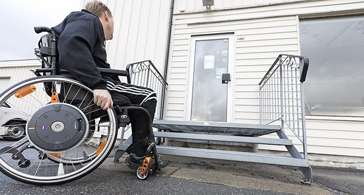 En person i rullstol framför ett hus med en trappa.