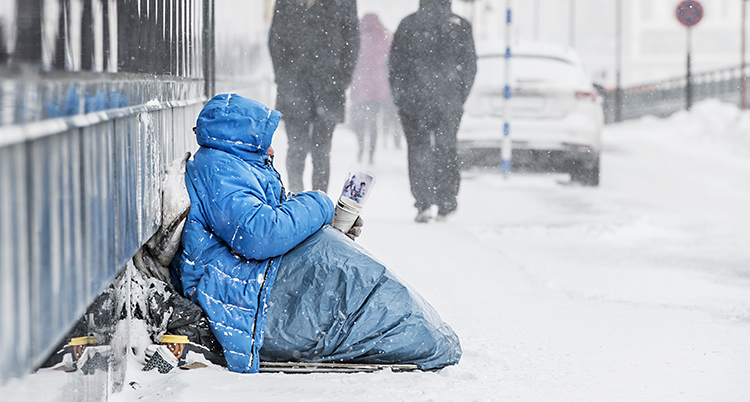 En tiggare sitter på en gata full med snö.