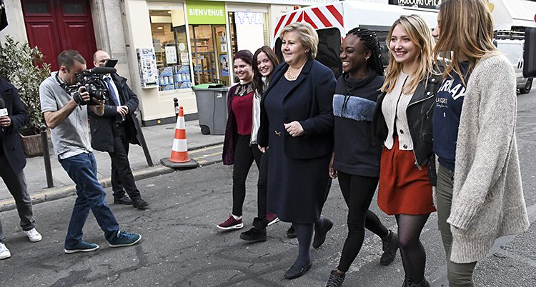 Skådespelarna går på en gata och hoåller om varandra och ler tillsammans med Erna Solberg.