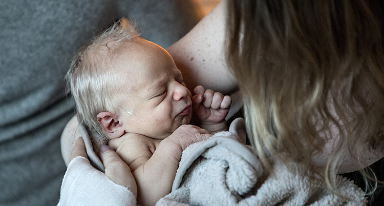 En nyfödd bebis vilar en kvinnas famn.