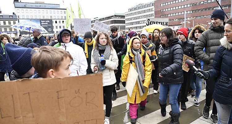 Greta och flera andra i regnkläder följs av journalister.