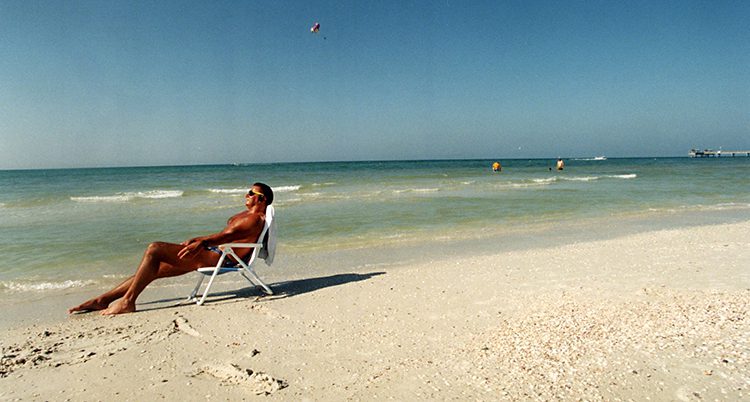 En solbränd man sitter och solar på en strand