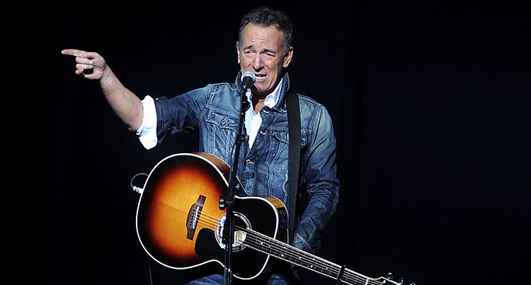 Bruce Springsteen sjunger i en mikrofon med en gitarr på magen.