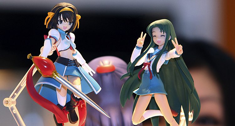 Två typiska animefigurer, flickor i skoluniformer. De ser självsäkra ut, en har ett svärd, en annan gör v-tecknet i luften. 