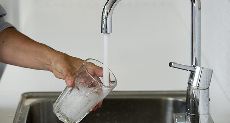 En arm sträcker fram ett glas under en kran. Från kranen rinner det vatten ner i glaset.
