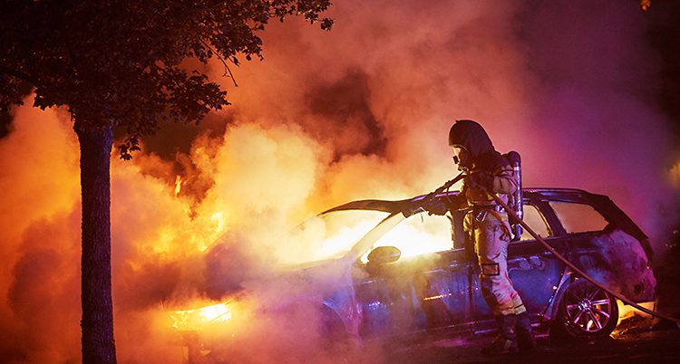 Rök och eld kommer från bilen. En brandman sprutar vatten.