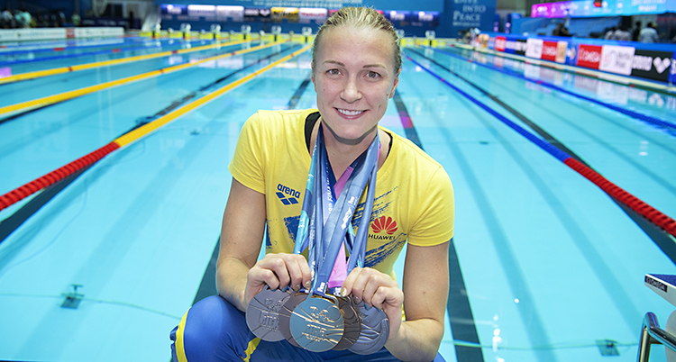 Simmaren Sarah Sjöström står vid en bassäng och visar sina fem medaljer.