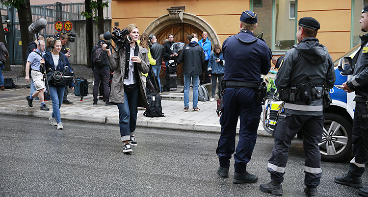 Poliser, en kvinna med kamera och andra människor utanför ett gult stenhus