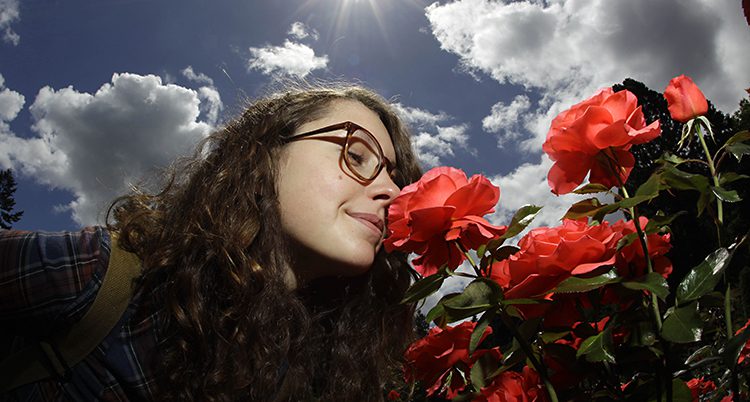 En kvinna med glasögon luktar på rosor i en park.