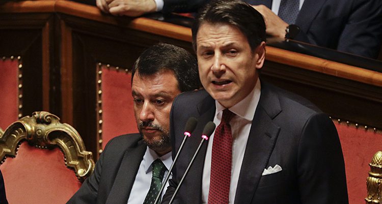 Ganska nära bild på båda männen. Conte ser bestämd ut när han pratar in i mikrofonen. Salvini tittar ner och ser dyster ut.