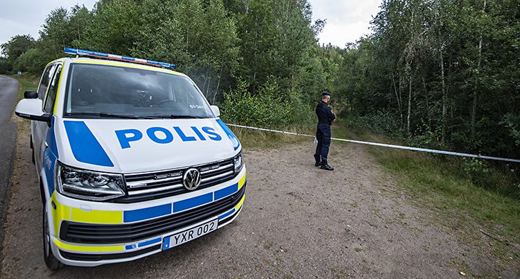 En polisbil och en polis står vid en vägkant. Där finns ett avspärrningsband och på andra sidan bandet är en skog.