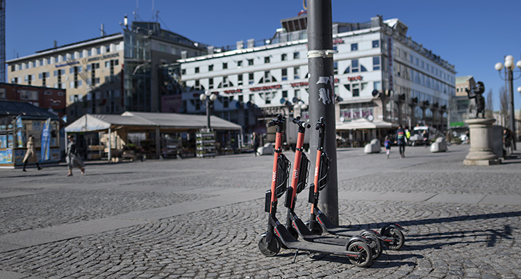 Tre sparkcyklar står vid en lyktstolpe på ett torg i Stockholm