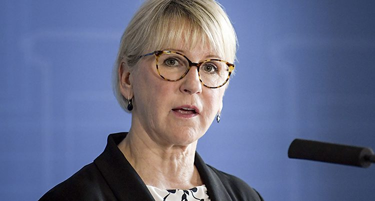 Margot Wallström pratar med journalister i Sverige. Hon har glasögon på sig, och pratar i en mikrofon. Det är en blå vägg bakom.