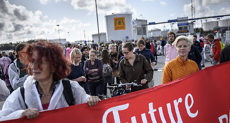 Många människor har samlats i hamnen. Två kvinnor håller i en banderoll med ordet Future i vit text.