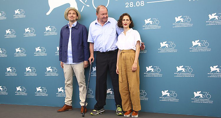 De tre står bredvid varandra och ler. På väggen bakom dem är reklam för filmfestivalen i Venedig.