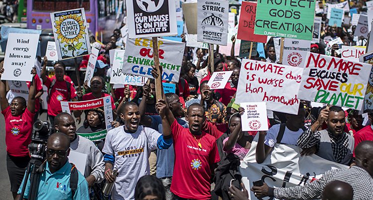 Många unga personer trängs, ropar och håller upp skyltar med budskap på engelska om klimatet.
