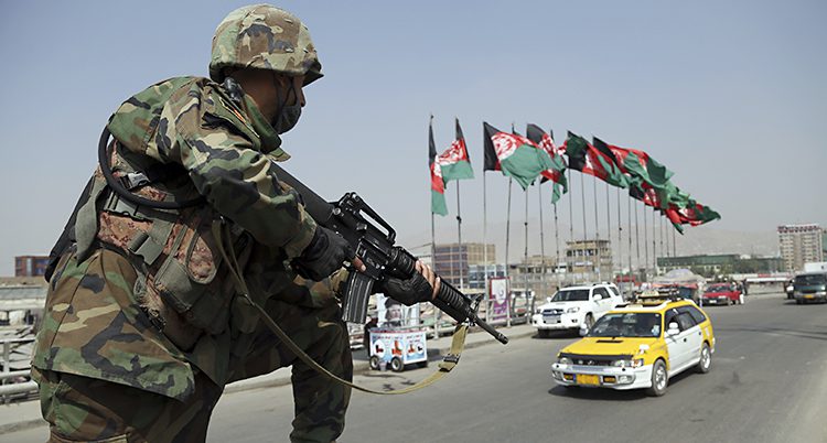 En soldat med vapen vaktar en gata med bilar och afghanska flaggor