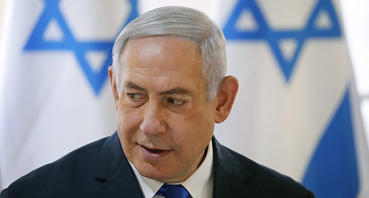 Benjamin Netanyahu har kostym på sig. I bakgrunden syns Israels flagga i vitt och blått.