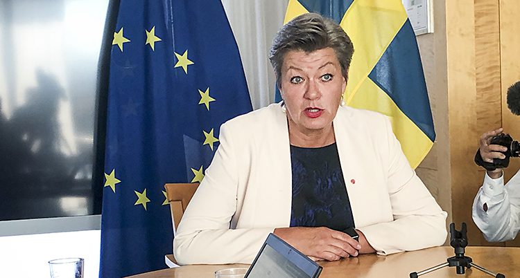 Ylva Johansson pratar. Hon sitter vid ett skrivbord fram en svensk flagg och EUs flagga.